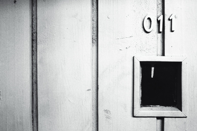 Detail image of a wooden, sloppily painted door. On the right is a small spyhole to view into the room with the room number 011 in raised lettering above it.